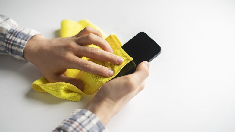 A person cleaning a smartphone screen with a bright yellow microfiber cloth.